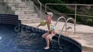 穿着袖子和帽子的小男孩在度假时跳进游泳池。 男孩在热带的游泳池里游泳。 儿童潜水